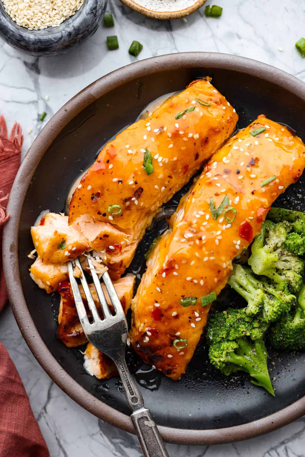 Bang Bang Salmon takes salmon filets, smothered in bang bang sauce, which is sweet with a kick, and then baked to perfection. You will love this simple yet oh-so-tasty dinner that can beย ready to serve in less than 30 minutes! Overhead shot of plated bang bang salmon next to broccoli.
