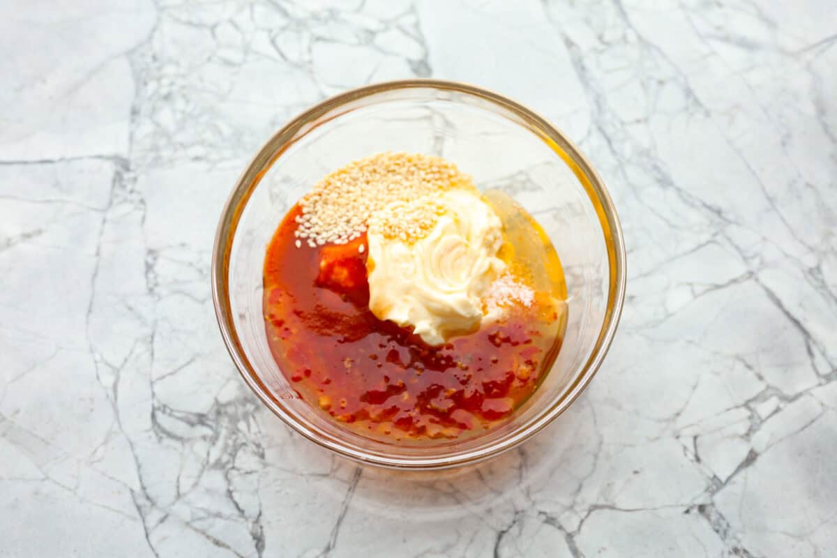 Bang Bang Salmon takes salmon filets, smothers them in bang bang sauce that is sweet with a kick, and then baked to perfection. You will love this simple yet oh-so-tasty dinner that can be ready to serve in less than 30 minutes! Overhead shot of sauce ingredients in a glass bowl.