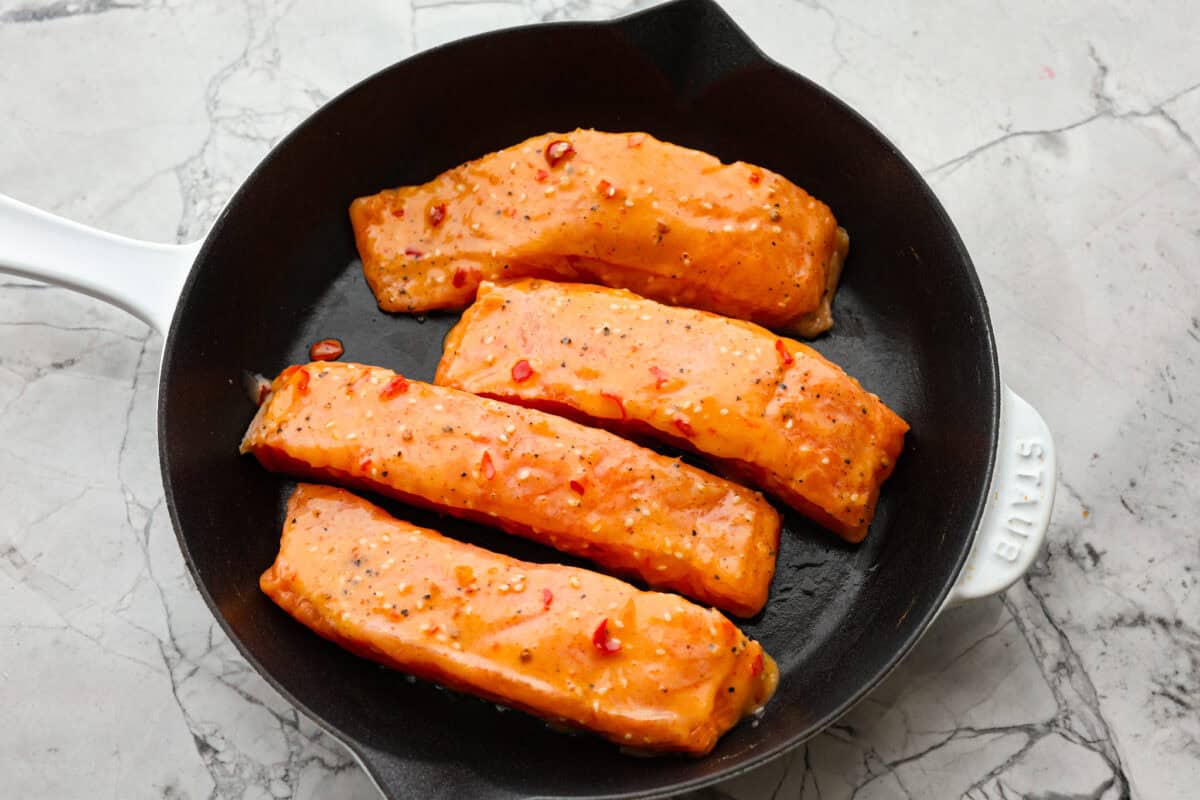 Bang Bang Salmon takes salmon filets, smothers them in bang bang sauce that is sweet with a kick, and then baked to perfection. You will love this simple yet oh-so-tasty dinner that can be ready to serve in less than 30 minutes! Overhead shot of salmon filets in a skillet.