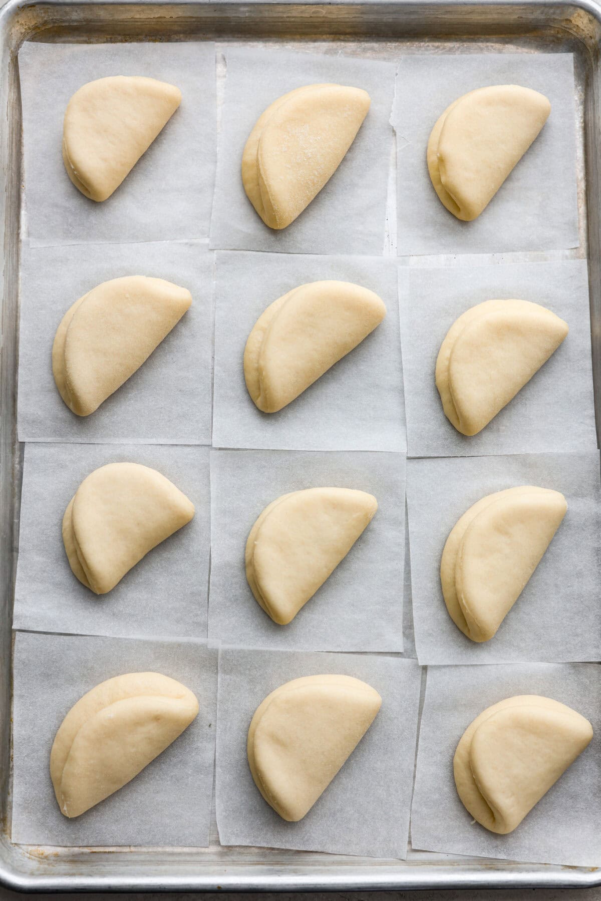 Bao Buns, or Baozi, are soft, pillowy buns made from a slightly sweet dough. They originate from China and are served with different types of fillings. You can enjoy them as a snack, as a side, or with dim sum. Overhead shot of bao bun dough circles folded in half on individual parchment papers on a cookie sheet.