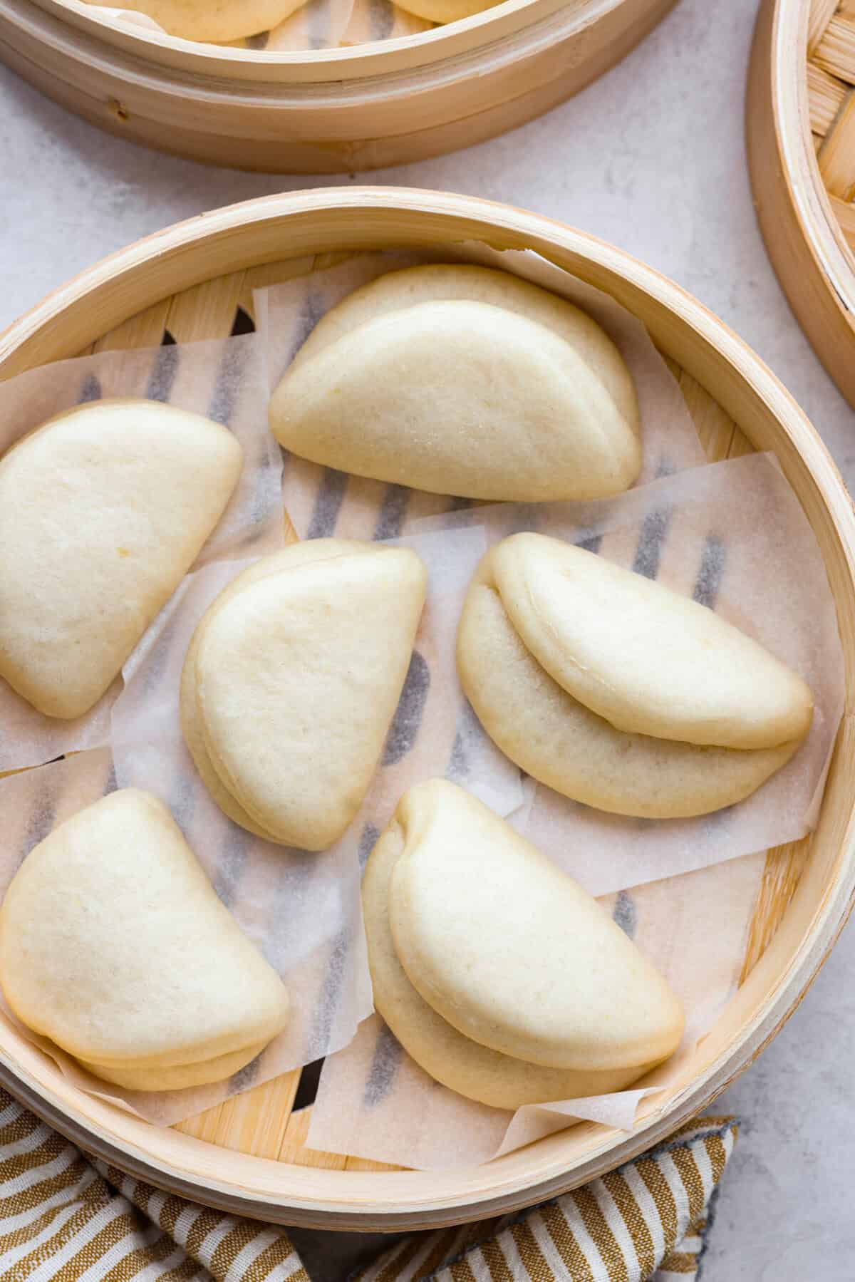 Bao Buns, or Baozi, are soft, pillowy buns made from a slightly sweet dough. They originate from China and are served with different types of fillings. You can enjoy them as a snack, as a side, or with dim sum. Overhead shot of cooked bao buns in a bamboo steamer.