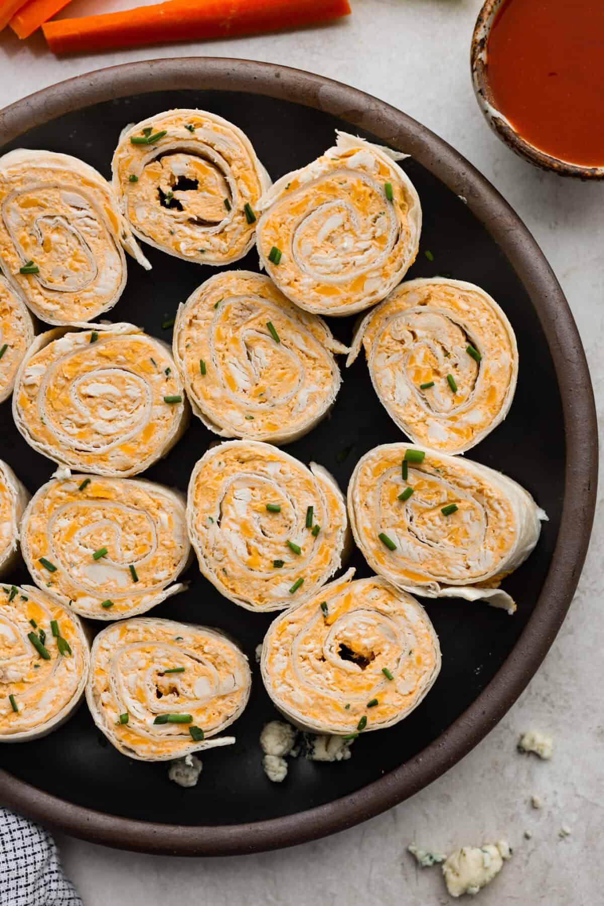 These zesty Buffalo Chicken Pinwheels are an easy snack or appetizer that everyone will devour! A creamy buffalo-flavored spread full of shredded chicken, seasonings, and cheeses all rolled inside of a soft tortilla. Slice into cute pinwheels and enjoy! Top view of buffalo chicken pinwheels on a black plate.