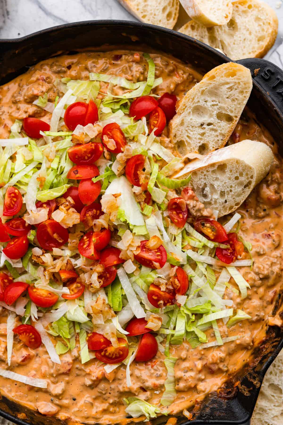 Cheeseburger dip is a crowd-pleasing appetizer for potlucks, parties, and get-togethers! This recipe takes delicious cheeseburger ingredients like beef, onion, tomato, relish, and cheese and turns them into a deliciously addicting snack! Close up shot of cheeseburger dip.