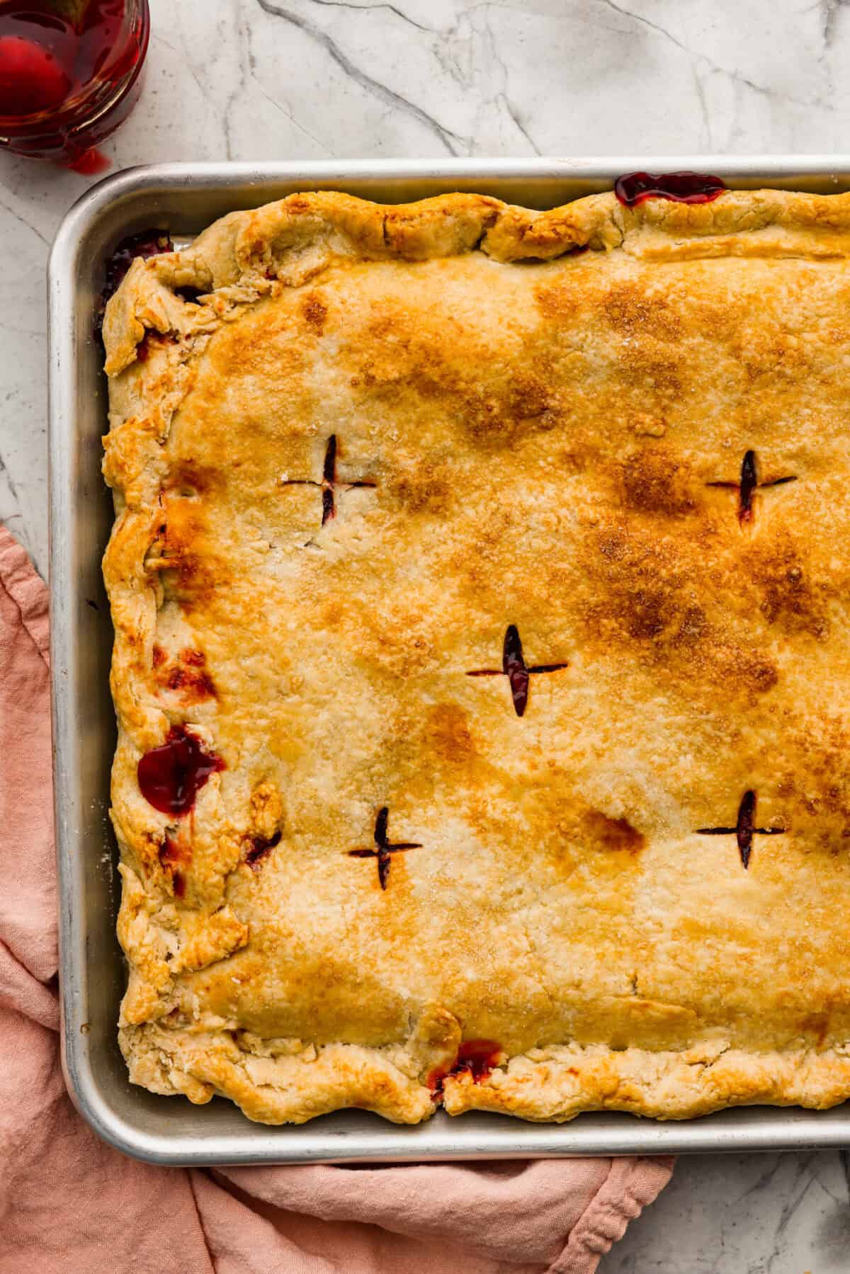 Cherry Slab Pie is an American classic made to serve a crowd! This recipe uses a tender, flaky crust that surrounds sweet, juicy cherry pie filling. It tastes incredibly delicious and is the perfect dessert for any time of year. Close up shot of baked cherry pie slab just out of the oven.