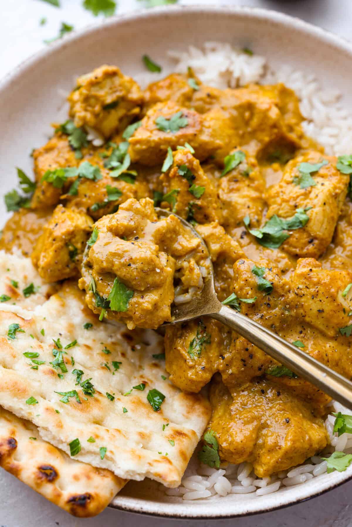 Chicken korma is a traditional Indian chicken dish. It's made with tender chicken smothered in a creamy, wonderfully seasoned sauce. It's so good your family will think you got takeout! Close up shot of plated chicken korma with a bite on a gold spoon.
