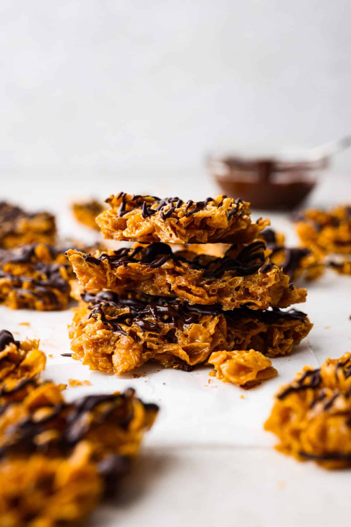 This cornflake brittle crack is crispy, chewy and to die for! With only six ingredients and 8 minutes of prep, you can have this yummy treat ready in no time. This brittle is crunchy cornflakes mixed with a buttery caramel sauce and drizzled in rich dark chocolate. Side shot of stacked pieces of cornflake brittle crack.
