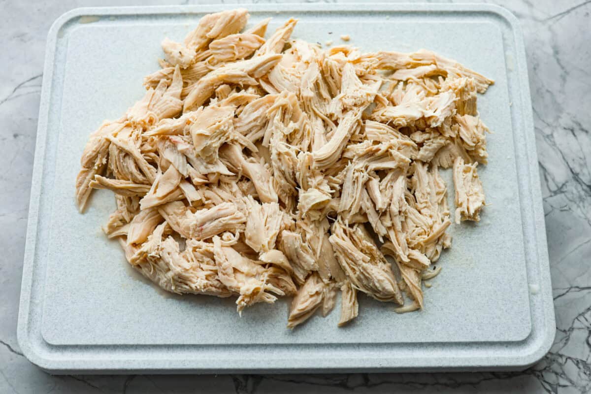 This crockpot chicken alfredo is a family dinner that's packed with flavor! The juicy, tender chicken cooked with creamy, cheesy pasta simply can't be beat! Plus, it’s super easy when your crock pot does all the work! Overhead shot shredded chicken on a cutting board.