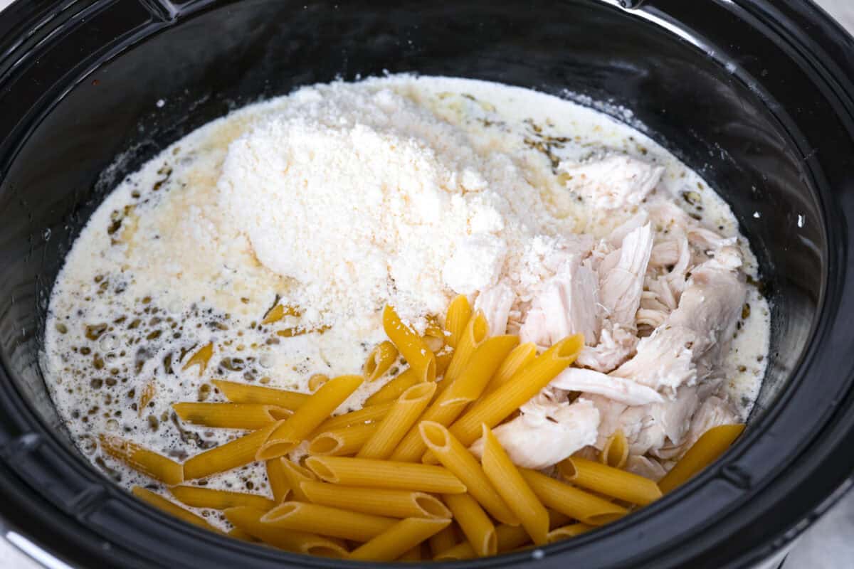 This crockpot chicken alfredo is a family dinner that's packed with flavor! The juicy, tender chicken cooked with creamy, cheesy pasta simply can't be beat! Plus, it’s super easy when your crock pot does all the work! Overhead shot of pasta, chicken and parmesan cheese added back into the crockpot.