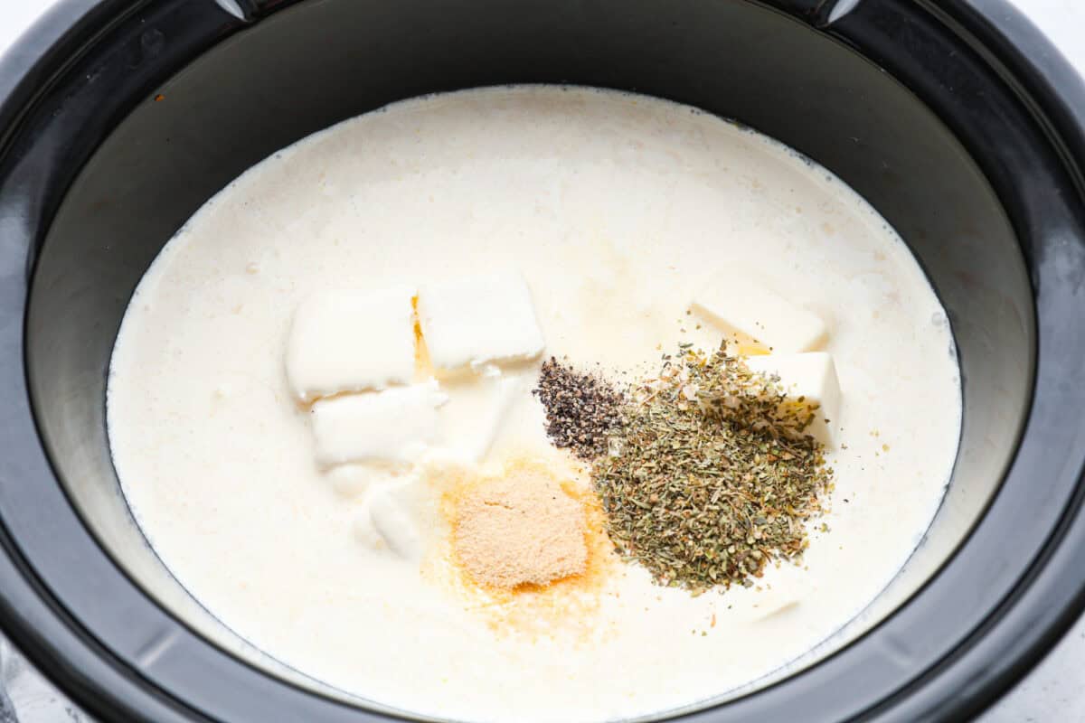 This crockpot chicken alfredo is a family dinner that's packed with flavor! The juicy, tender chicken cooked with creamy, cheesy pasta simply can't be beat! Plus, it’s super easy when your crock pot does all the work! Overhead shot of chicken in the crockpot with seasonings, whipping cream, chicken broth, butter and cream cheese added on top.
