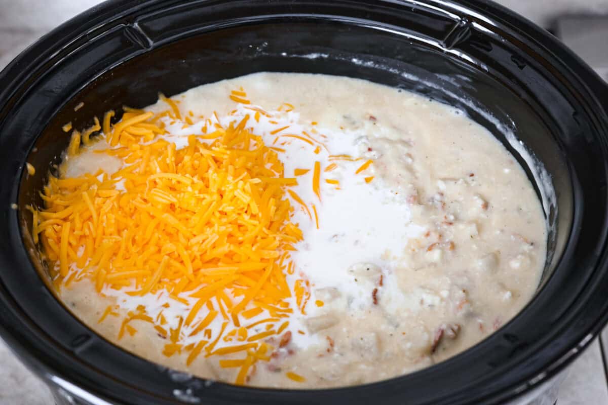 This crock pot crack potato soup is the best and easiest soup you will ever make! It's loaded with creamy cheese, potatoes, hearty chicken, and savory bacon, all seasoned to perfection! Your family will love smelling this cooking when they get home from school! They will like how it tastes even better! Overhead shot of cheese and half and half on top of mixed soup in crock pot.