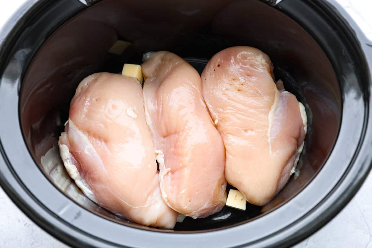 Crockpot buffalo chicken chili is a buffalo wing lover's dream. It has a tangy, fiery buffalo hot sauce base mixed with shredded chicken, smooth cream cheese, tender beans, and vegetables. If you love buffalo wings, you will love this chili! Overhead shot of chicken breasts and butter in the bottom of the crockpot.