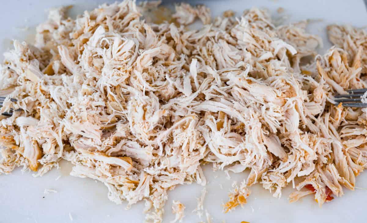 Crockpot buffalo chicken chili is a buffalo wing lover's dream. It has a tangy, fiery buffalo hot sauce base mixed with shredded chicken, smooth cream cheese, tender beans, and vegetables. If you love buffalo wings, you will love this chili! Angle shot of chicken shredded on a cutting board.