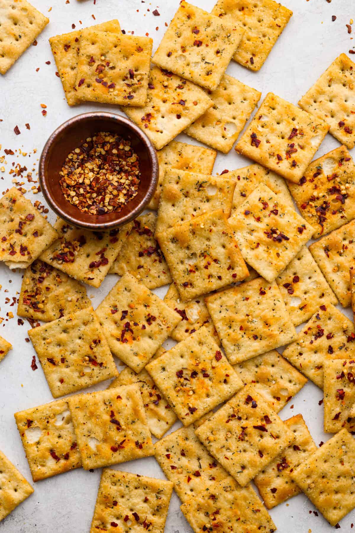Get the party started with Fire Crackers! In this recipe, saltine crackers are transformed from something ordinary into something extraordinary with a flavorful blend of seasonings. They're easy to make and perfect for snacking on around the holidays (or anytime)! Overhead shot of fire crackers on a counter top with a bowl of red pepper flakes in a small bowl.