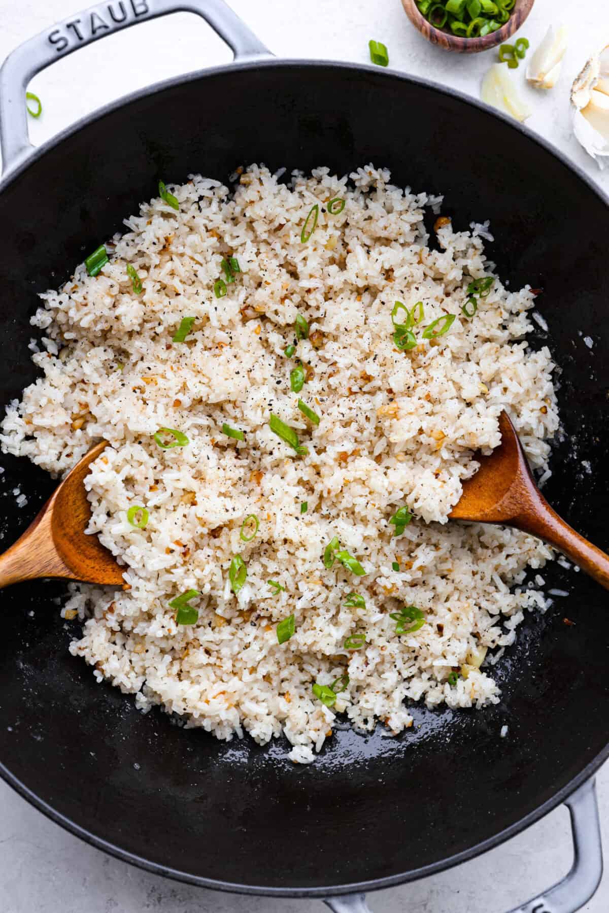 Garlic fried rice is one of the most common Filipino rice dishes. It combines leftover rice with crispy fried garlic, all tossed together with seasonings to create something simple that is incredibly flavorful! Overhead shot of garlic fried rice in a walk with two wooden spoons.