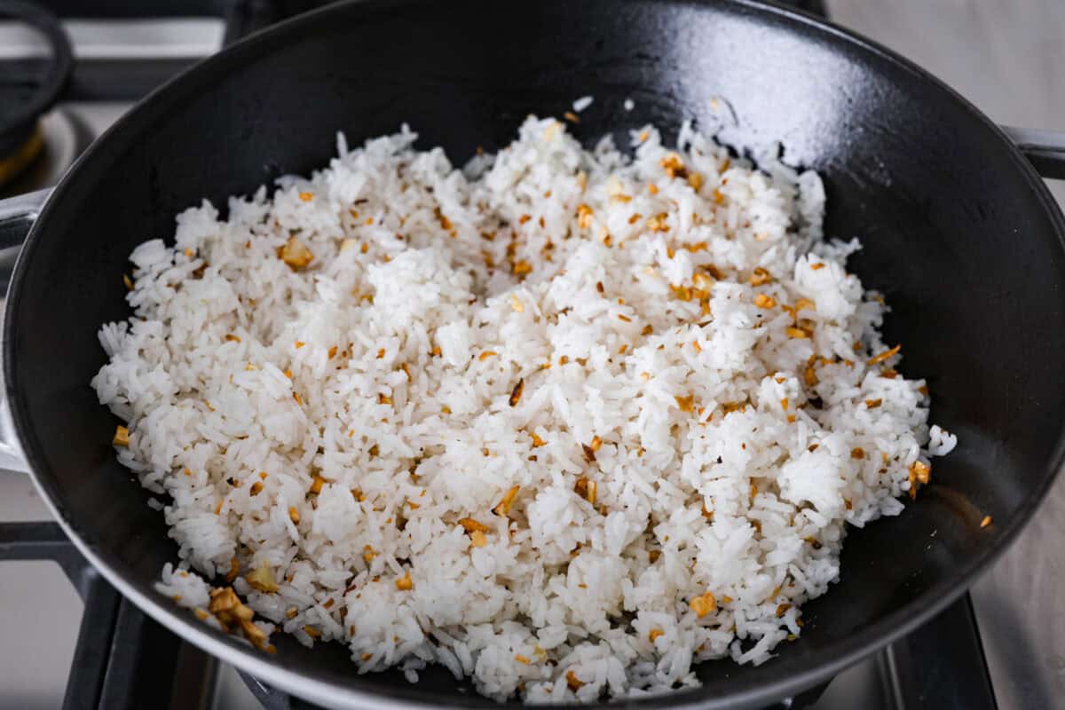 Garlic fried rice is one of the most common Filipino rice dishes. It combines leftover rice with crispy fried garlic, all tossed together with seasonings to create something simple that is incredibly flavorful! Angle shot of rice added to the pan.