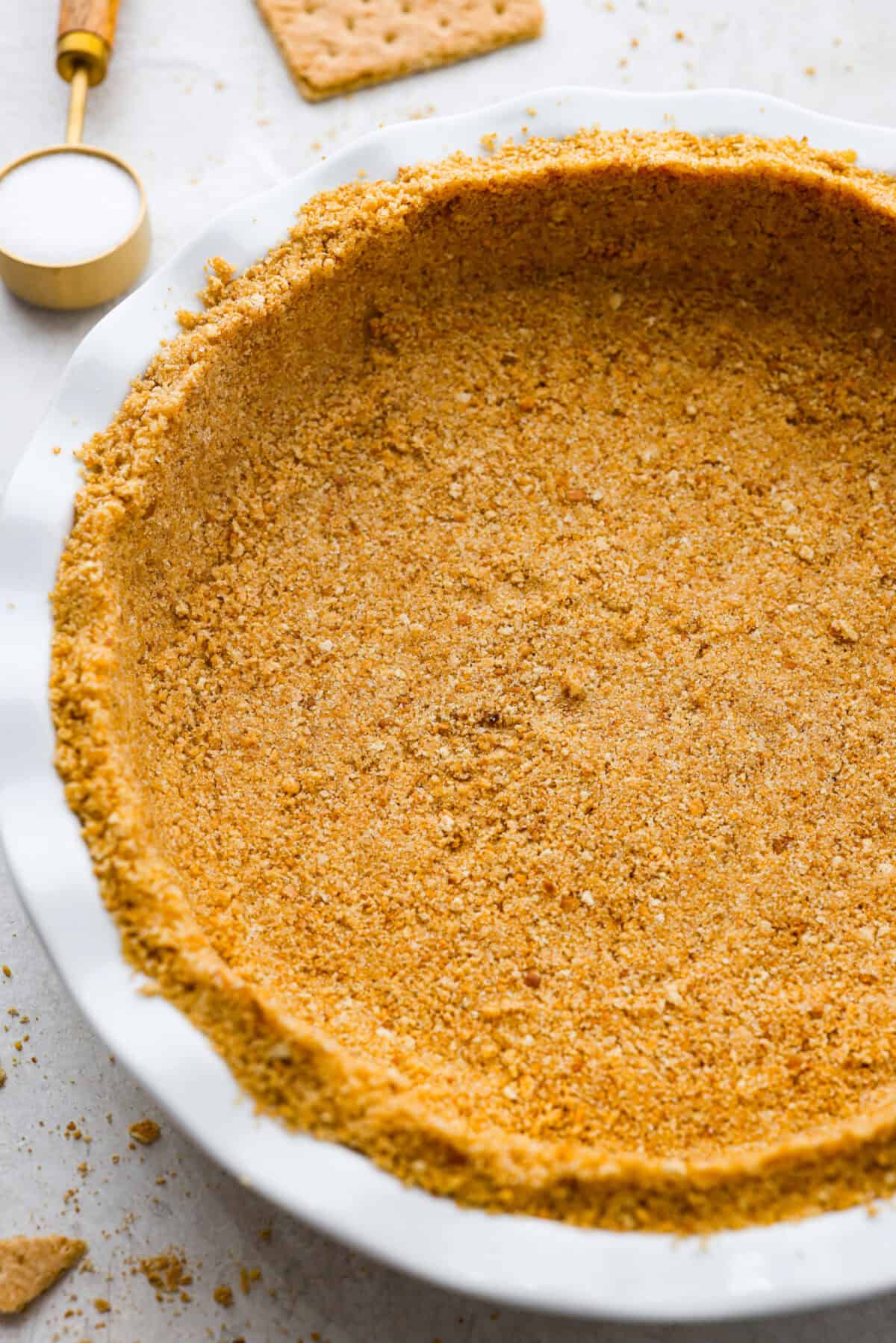 Learn how to make the perfect homemade Graham Cracker Crust! It comes together in just 10 minutes with 3 simple ingredients for the right amount of buttery sweetness and crunch!ย Youโll never buy one from the store again! Close up shot of the graham cracker crust.