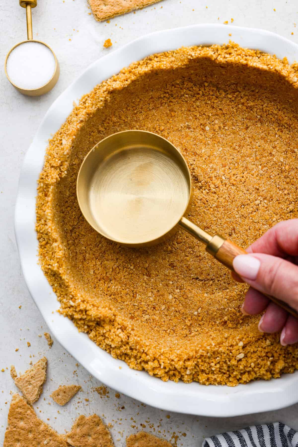 Learn how to make the perfect homemade Graham Cracker Crust! It comes together in just 10 minutes with 3 simple ingredients for the right amount of buttery sweetness and crunch!ย Youโll never buy one from the store again! Overhead shot of someone pressing a measuring cup into the homemade graham cracker crust.