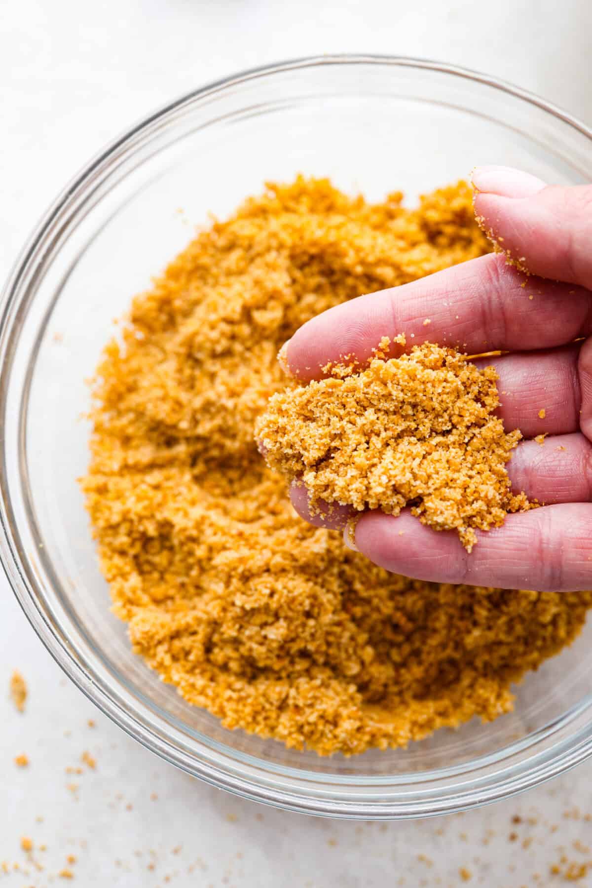 Learn how to make the perfect homemade Graham Cracker Crust! It comes together in just 10 minutes with 3 simple ingredients for the right amount of buttery sweetness and crunch!ย Youโll never buy one from the store again! Overhead shot of someone holding a handful of the crust mixture.