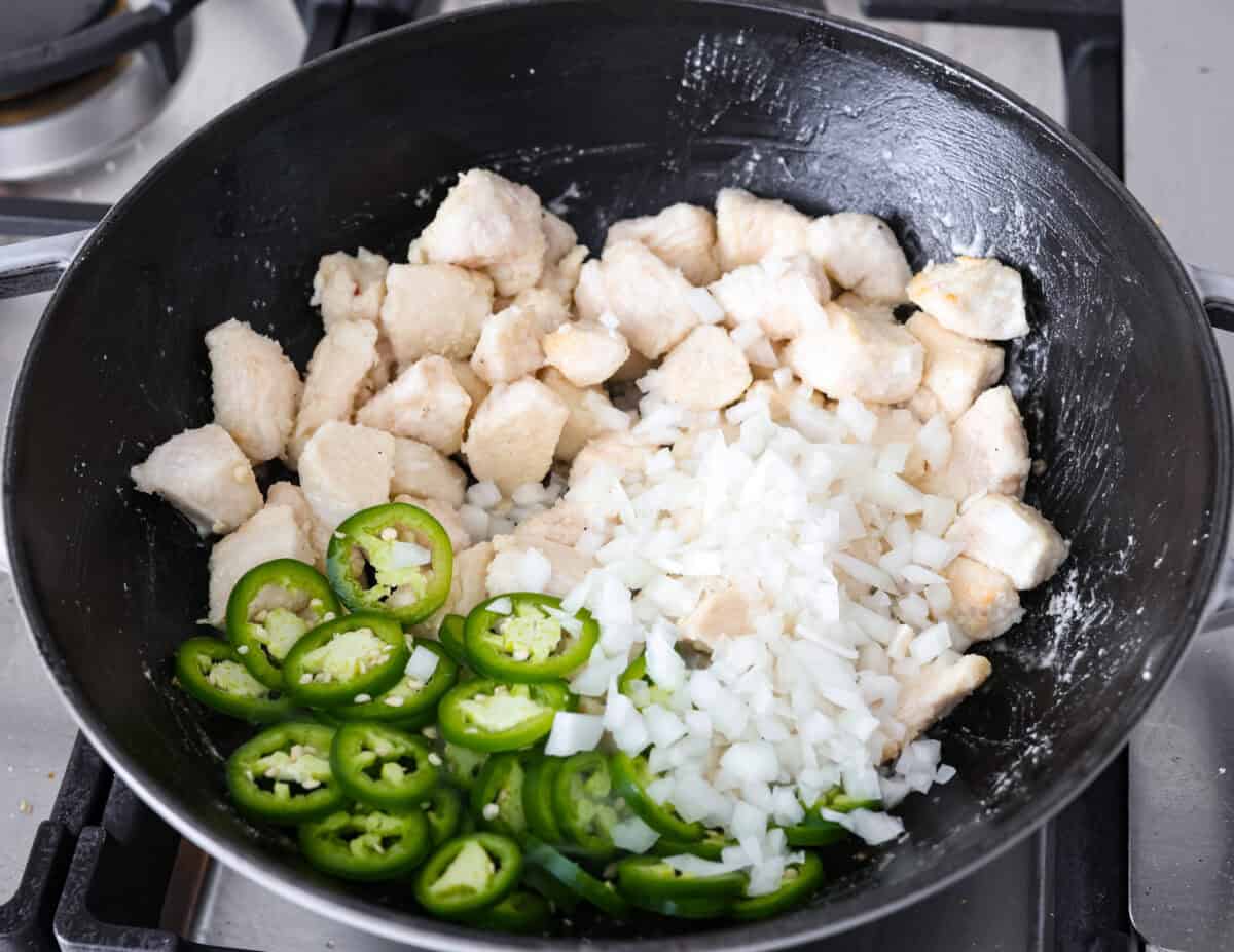 Delicious Jalapeño Chicken will become an instant favorite with the very first bite. Tender chicken pieces are cooked with jalapeños and then coated in a sticky, sweet, and spicy sauce. Serve over rice for an easy meal. You'll be craving it on repeat! Angle shot of chicken jalapeños and onions in a skillet.