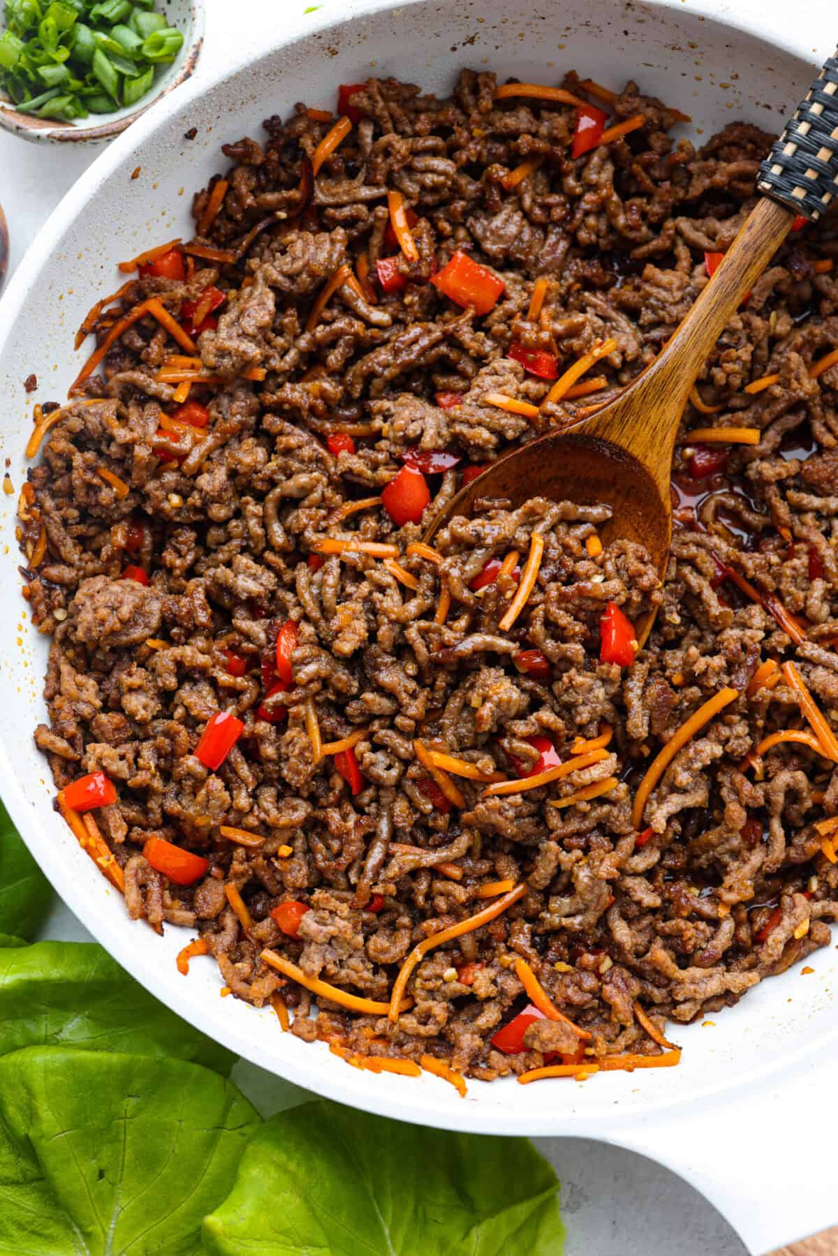 Enjoy delicious Asian flavors in these Korean Beef Lettuce Wraps! This appetizer or main is loaded with tasty lean ground beef, sautรฉed shredded carrots, red bell pepper, and garlic, all tossed in a mouthwatering sauce and spooned into lettuce leaves. Overhead shot of Korean beef lettuce wrap beef and vegetable mixture in a skillet.