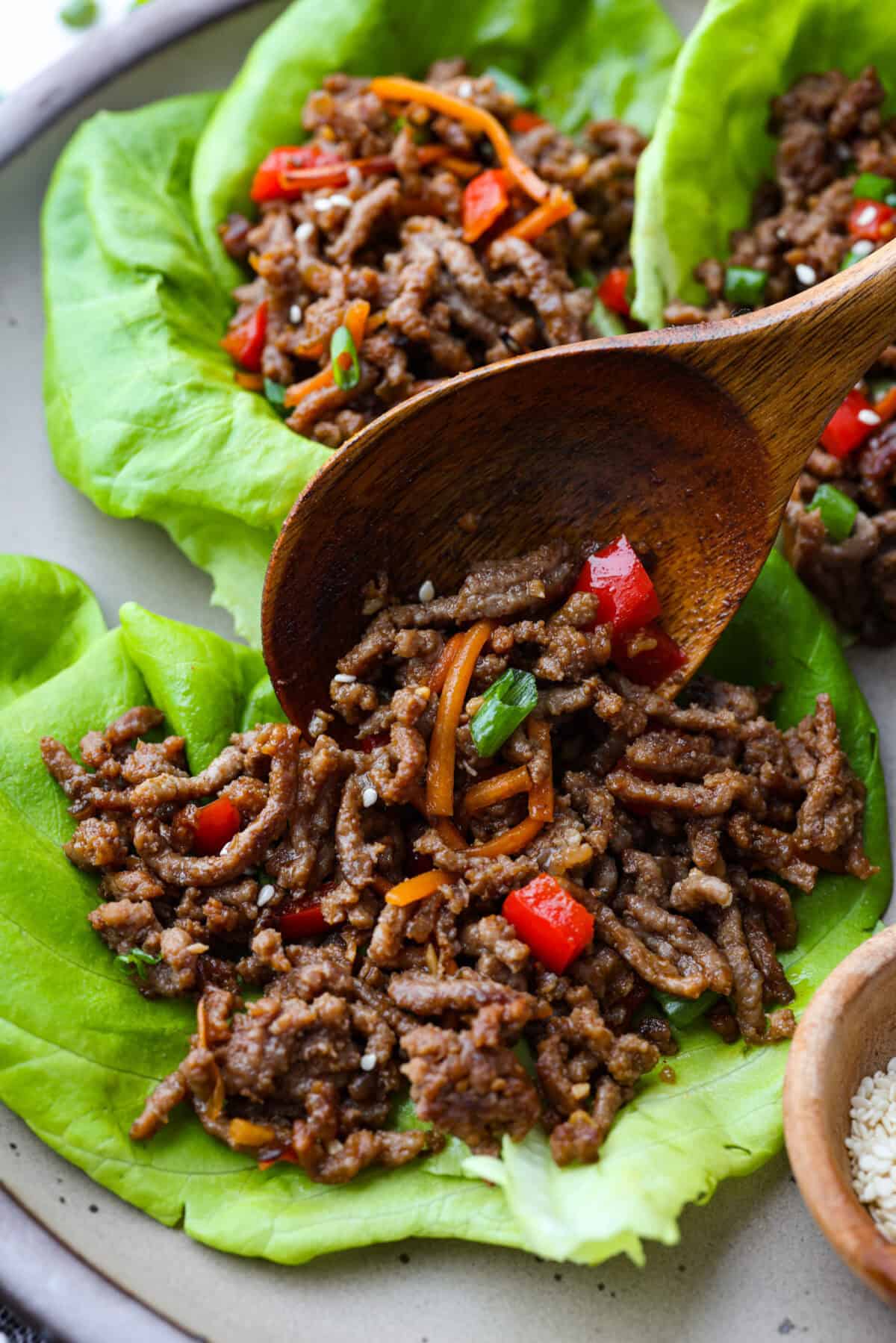 Enjoy delicious Asian flavors in these Korean Beef Lettuce Wraps! This appetizer or main is loaded with tasty lean ground beef, sautรฉed shredded carrots, red bell pepper, and garlic, all tossed in a mouthwatering sauce and spooned into lettuce leaves. Close up shot of Korean beef lettuce wraps being assembled.