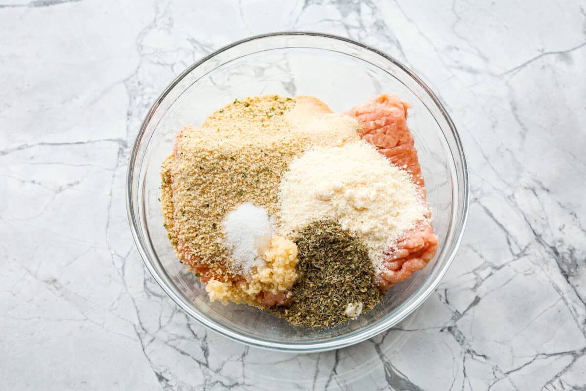 With creamy Tuscan flavors, these Marry Me Meatballs are an instant crowd favorite! It doesn't get much better than Italian seasoned chicken meatballs nestled in a creamy, cheesy sauce with sun-dried tomatoes and fresh herbs. Overhead shot of meatball ingredients dumped in a glass bowl.