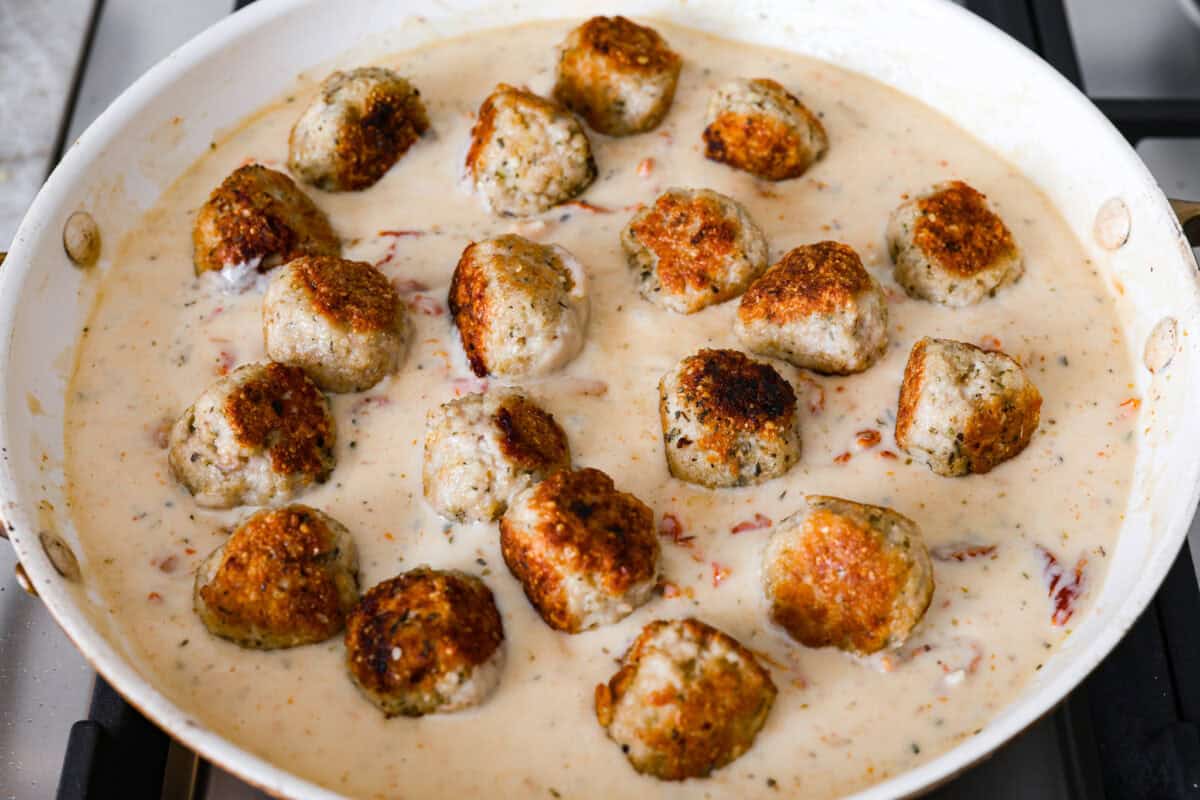 With creamy Tuscan flavors, these Marry Me Meatballs are an instant crowd favorite! It doesn't get much better than Italian seasoned chicken meatballs nestled in a creamy, cheesy sauce with sun-dried tomatoes and fresh herbs. Overhead shot of the meatballs added back to the pan.