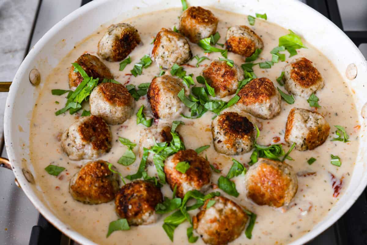 With creamy Tuscan flavors, these Marry Me Meatballs are an instant crowd favorite! It doesn't get much better than Italian seasoned chicken meatballs nestled in a creamy, cheesy sauce with sun-dried tomatoes and fresh herbs. Overhead shot of meatballs and sauce in a pan with basil sprinkled over the top.