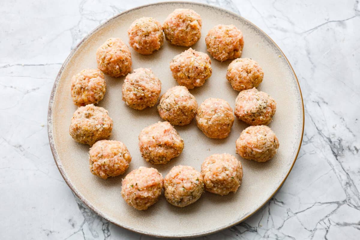 With creamy Tuscan flavors, these Marry Me Meatballs are an instant crowd favorite! It doesn't get much better than Italian seasoned chicken meatballs nestled in a creamy, cheesy sauce with sun-dried tomatoes and fresh herbs. Overhead shot of meatballs formed on a plate.
