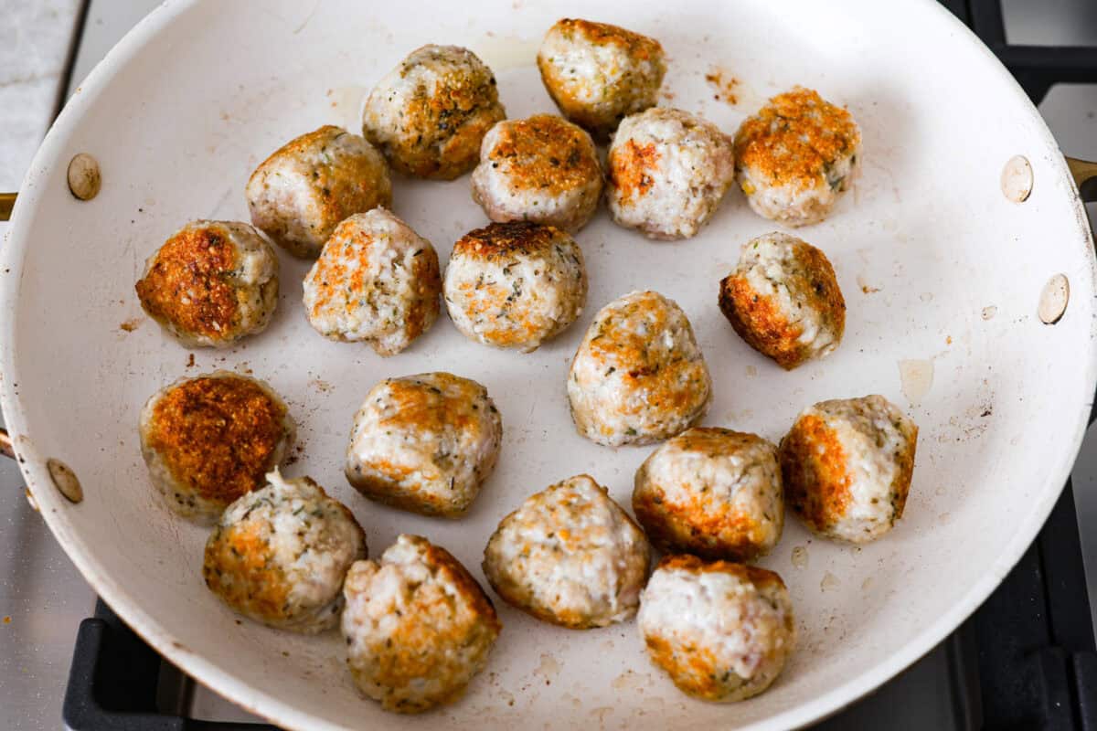 With creamy Tuscan flavors, these Marry Me Meatballs are an instant crowd favorite! It doesn't get much better than Italian seasoned chicken meatballs nestled in a creamy, cheesy sauce with sun-dried tomatoes and fresh herbs. Overhead shot of meatballs browning in a skillet.