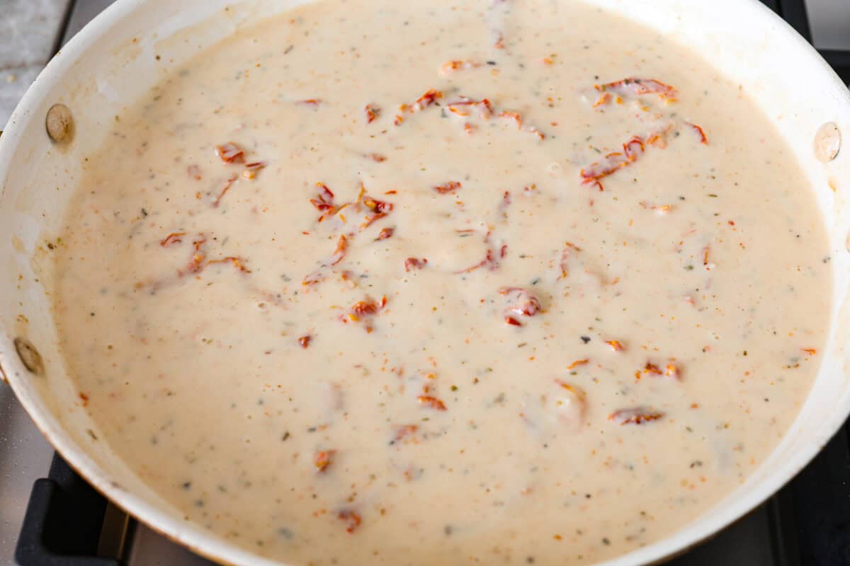 With creamy Tuscan flavors, these Marry Me Meatballs are an instant crowd favorite! It doesn't get much better than Italian seasoned chicken meatballs nestled in a creamy, cheesy sauce with sun-dried tomatoes and fresh herbs. Overhead shot of sauce mixed together and simmering on the stove top.