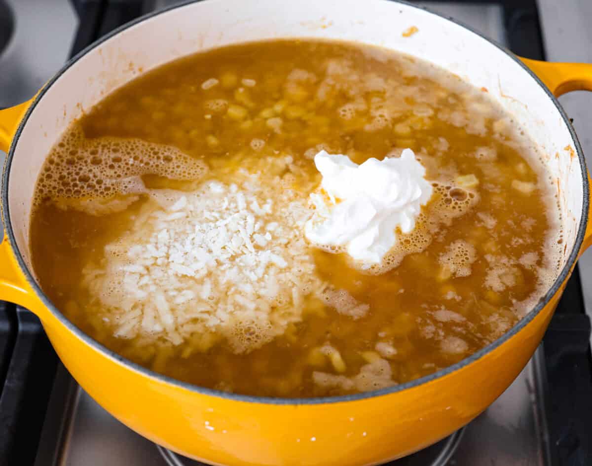 Mexican street corn soup has all the incredible flavors of street corn in a warm, comforting, delicious soup. This soup has fresh corn, lots of cotija cheese, spices, cilantro, lime juice, and sour cream to make it smooth and creamy. Angle shot of corn and onion mixture with vegetable broth, sour cream and cheese mixed in.