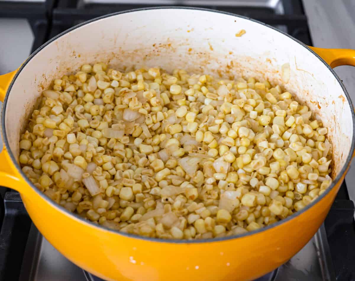 Mexican street corn soup has all the incredible flavors of street corn in a warm, comforting, delicious soup. This soup has fresh corn, lots of cotija cheese, spices, cilantro, lime juice, and sour cream to make it smooth and creamy. Angle shot of onion and corn in a pot cooking on the stove top.