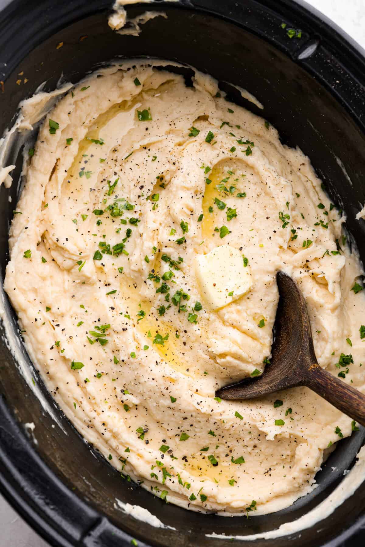 Million dollar mashed potatoes are unmatched when it comes to creamy velvety mashed potatoes. They get their intense flavors and smooth texture from letting the potatoes slow cook in chicken broth then mixing them with cream cheese, butter and garlic. Overhead shot of million dollar mashed potatoes with wooden serving spoon.