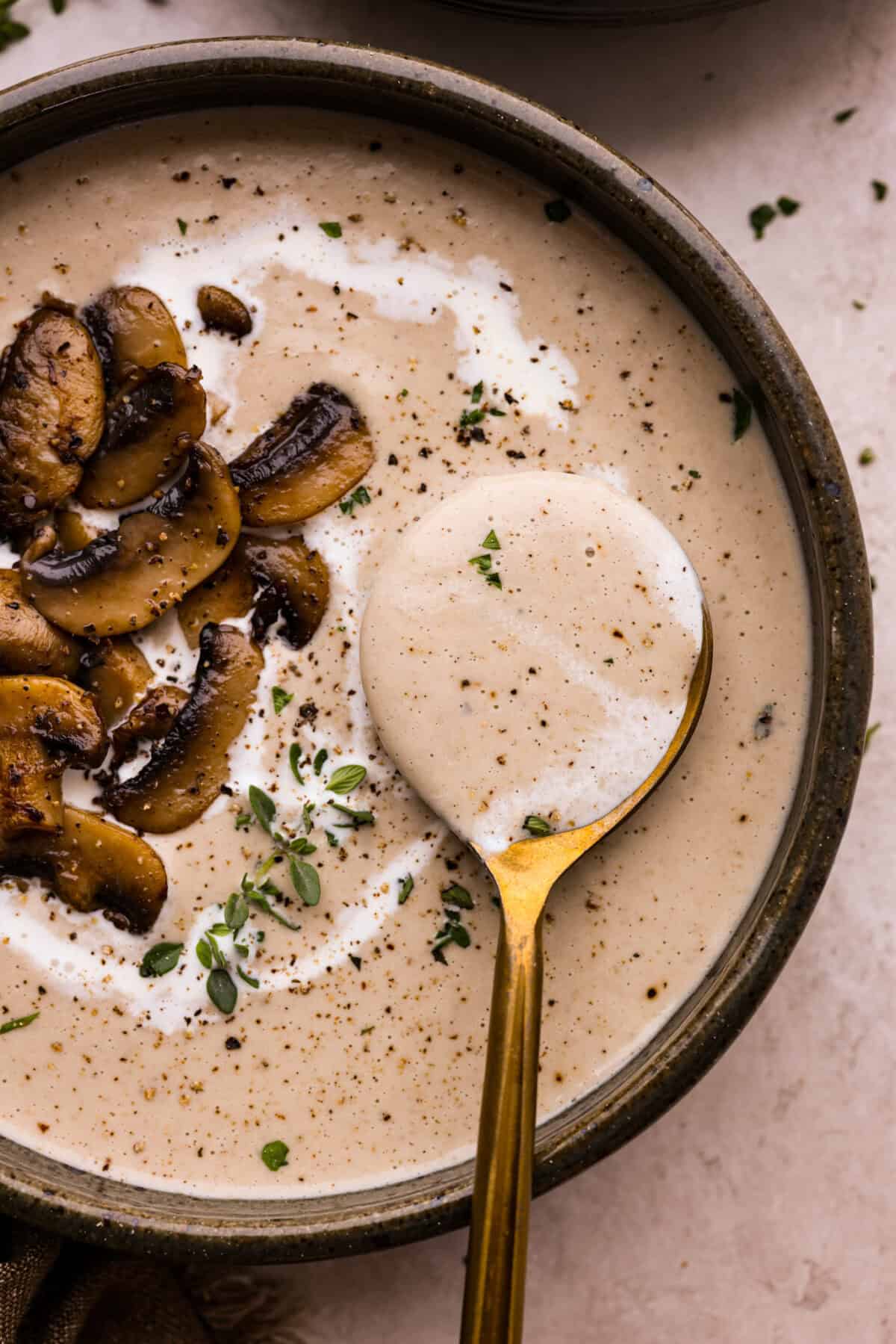 Mushroom bisque is full of cream and garlic-infused mushrooms, all blended to make a thick, rich, and beyond flavorful soup! You will want to drink this straight from your bowl! Overhead shot of a bowl of mushroom bisque with a spoon scooping out a bite.