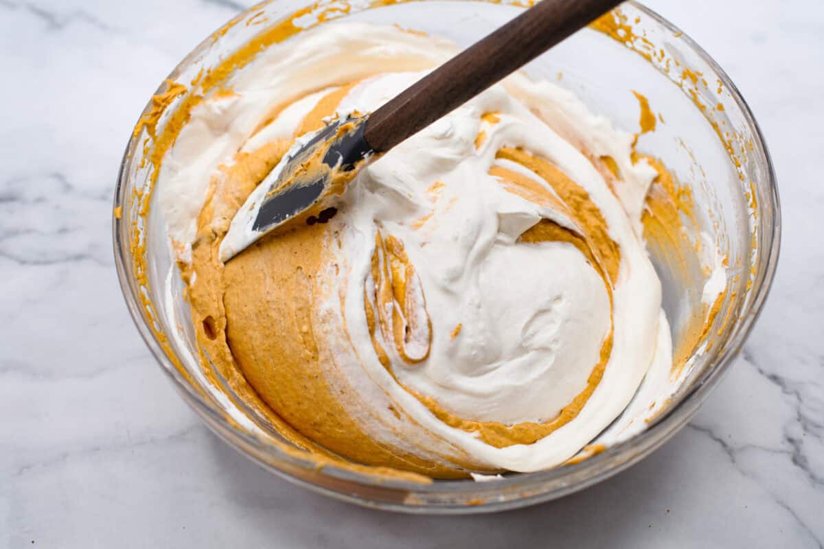 Delicious no-bake pumpkin cheesecake topped off with whipped cream is the perfect fall dessert. It has a creamy cheesecake filling with real pumpkin puree that sits in an irresistible Biscoff cookie crust.ย Itโs easy to make, rich, and perfectly spiced! Overhead shot of whipped cream being folded into the pumpkin mixture.