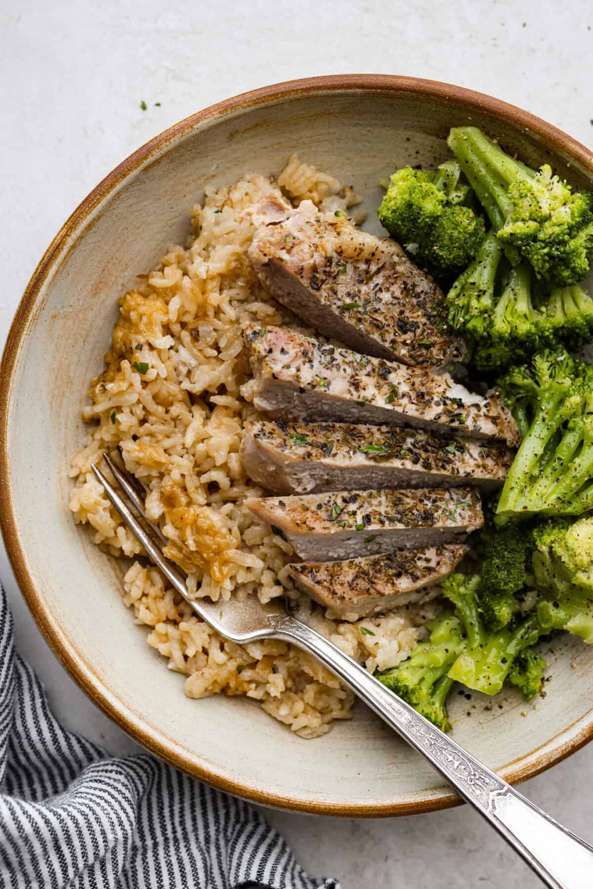 No Peek Pork Chops and Rice is comfort food at its best! Creamy, savory riceย and tender pork chops are baked together in the same pan with less than 10 minutes of prep. This dish is a go-to for busy weeknights and is perfect when you need a tasty meal without much hassle! Overhead shot of plated pork chops and rice with broccoli on the side.