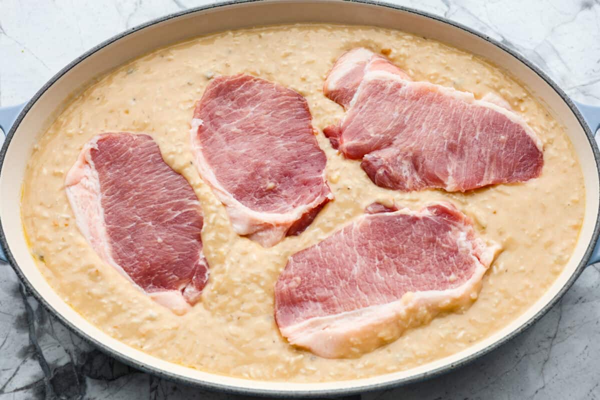 No Peek Pork Chops and Rice is comfort food at its best! Creamy, savory riceย and tender pork chops are baked together in the same pan with less than 10 minutes of prep. This dish is a go-to for busy weeknights and is perfect when you need a tasty meal without much hassle! Overhead shot of rice and soup mixture in the bottom of a baking dish with pork chops on top.