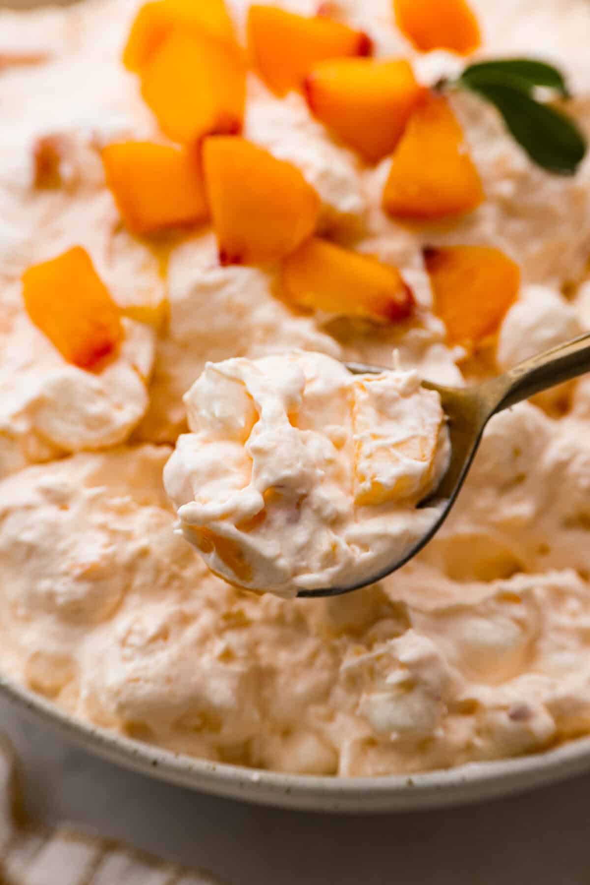 t's peach season which means you have to make this Peach Fluff Salad! It's a creamy, fruity dessert that hits all the right notes and is packed with fresh peaches! A close up of peach fluff salad on a spoon.