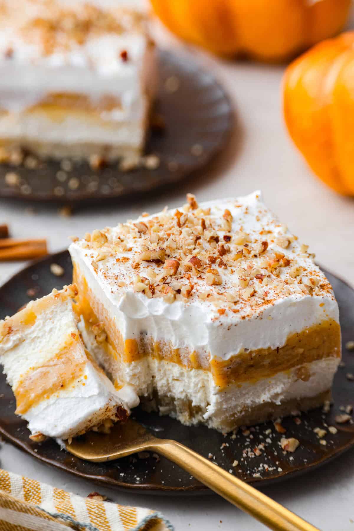 Fall in love with this Pumpkin Delight! A shortbread crust topped with a fluffy cheesecake mixture, a creamy pumpkin layer, and whipped topping. Every bite of this irresistible layered dessert is pumpkin heaven! Close view of a bite of pumpkin delight on a fork.