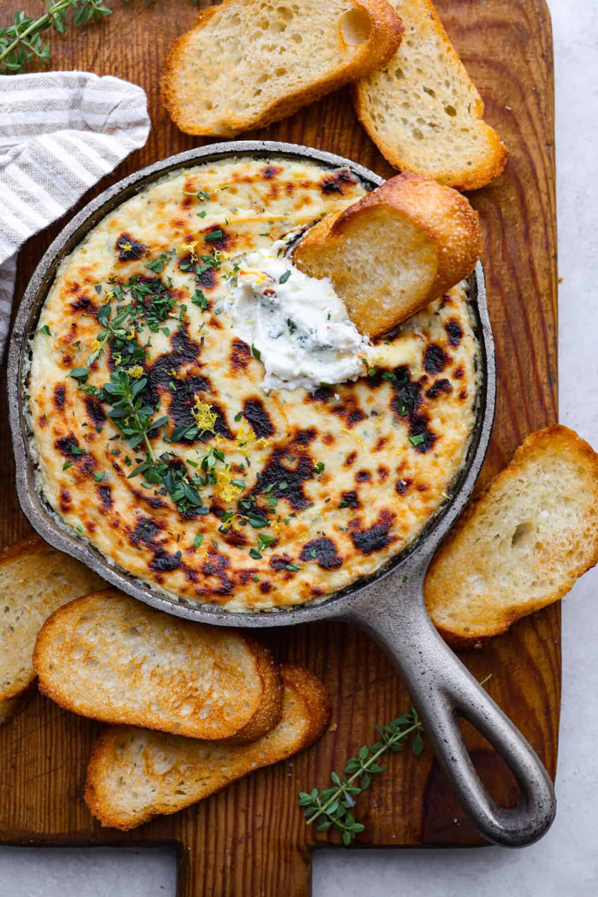Irresistible Baked Ricotta Dip is the perfect party appetizer! It takes just minutes to combine creamy ricotta cheese with parmesan, fresh herbs, and lemon zest. Then, bake until bubbly and delicious, and get ready for an explosion of flavor! Overhead shot of baked ricotta dip with a crostini in it.