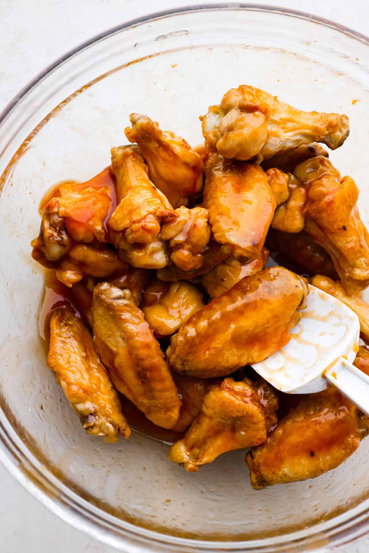 These sweet and sour wings are the perfect appetizer to serve for your next party, game day, or after-school snack. They are baked to crispy perfection and then doused in a sticky, sweet, and sour sauce. Close up shot of someone stirring wings covered in sweet and sour sauce in a glass bowl.