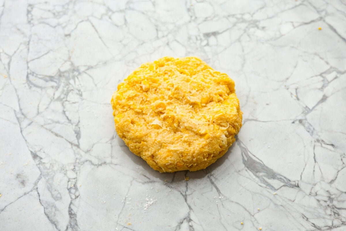 Homemade Sweet Corn Tamale Cakes are an explosion of delicious flavor in every bite! With this easy recipe you can bring this Cheesecake Factory favorite right to your own kitchen. Add the signature topping to really take these to the next level! Overhead shot of formed corn cake on a counter top.