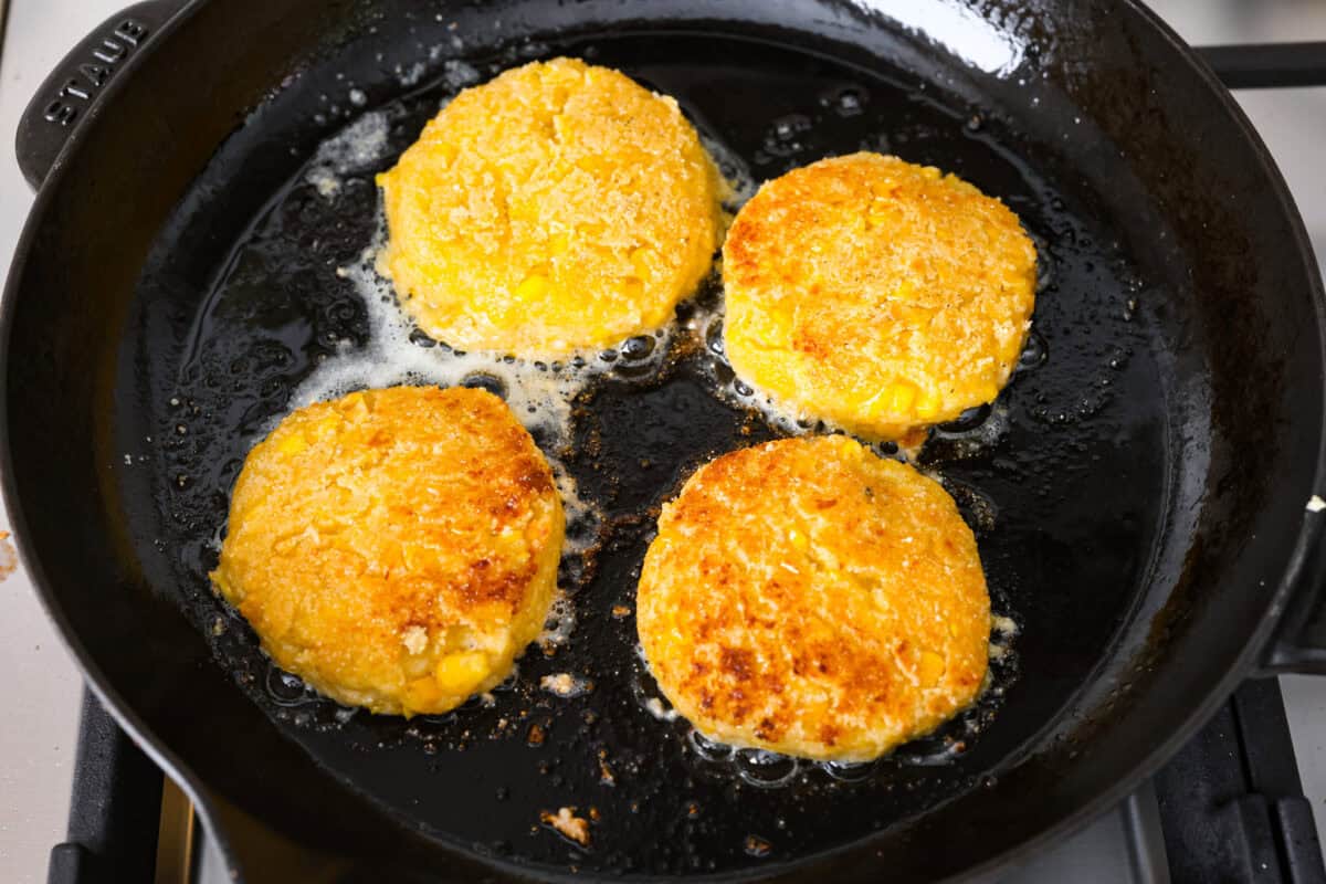 Homemade Sweet Corn Tamale Cakes are an explosion of delicious flavor in every bite! With this easy recipe you can bring this Cheesecake Factory favorite right to your own kitchen. Add the signature topping to really take these to the next level! Overhead shot of corn cakes frying in oil on a skillet.