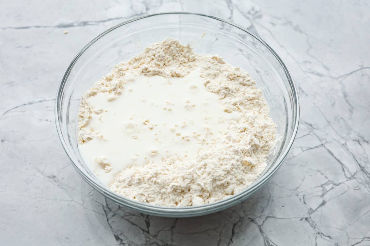 Cream cheese biscuits have a slight twist to the classic version. With the added cream cheese, they have a softer, more fluffy texture with an added tangy flavor that is so good! Overhead shot of flour, cream cheese and butt mixture with buttermilk poured over the top.