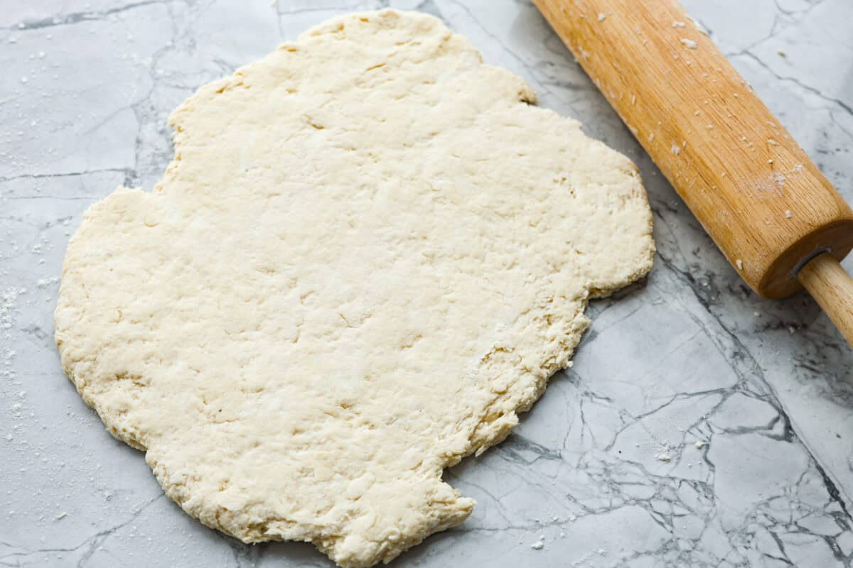 Cream cheese biscuits have a slight twist to the classic version. With the added cream cheese, they have a softer, more fluffy texture with an added tangy flavor that is so good! Overhead shot of the cream cheese biscuit dough rolled out next to a rolling pin.