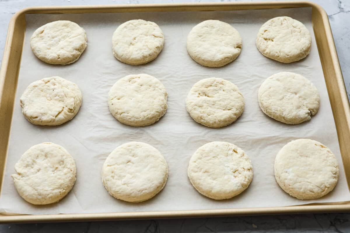 Cream cheese biscuits have a slight twist to the classic version. With the added cream cheese, they have a softer, more fluffy texture with an added tangy flavor that is so good! Angle shot of biscuit rounds on parchment paper on a baking sheet.