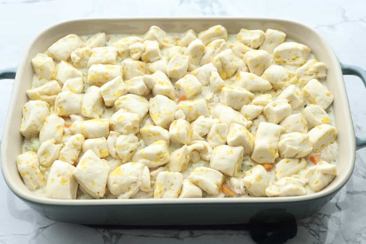 Chicken pot pie casserole is a fun twist on the classic pot pie. It's made with buttery biscuit dough, tender chicken, crunchy veggies, and the most delicious creamy sauce loaded with incredible seasoning. Comfort food at its finest! Angle shot of chicken pot pie casserole with biscuit pieces on top.