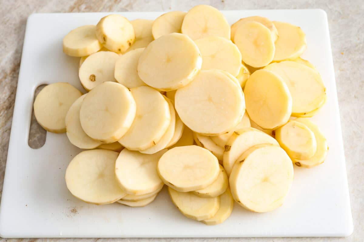 Hamburger Potato Casserole is hearty, filling, and great for family dinners. It's full of tender potatoes and ground beef, smothered in a deliciously creamy sauce, and covered in melty cheese. Overhead shot of a pile of thinly sliced potatoes on a cutting board.