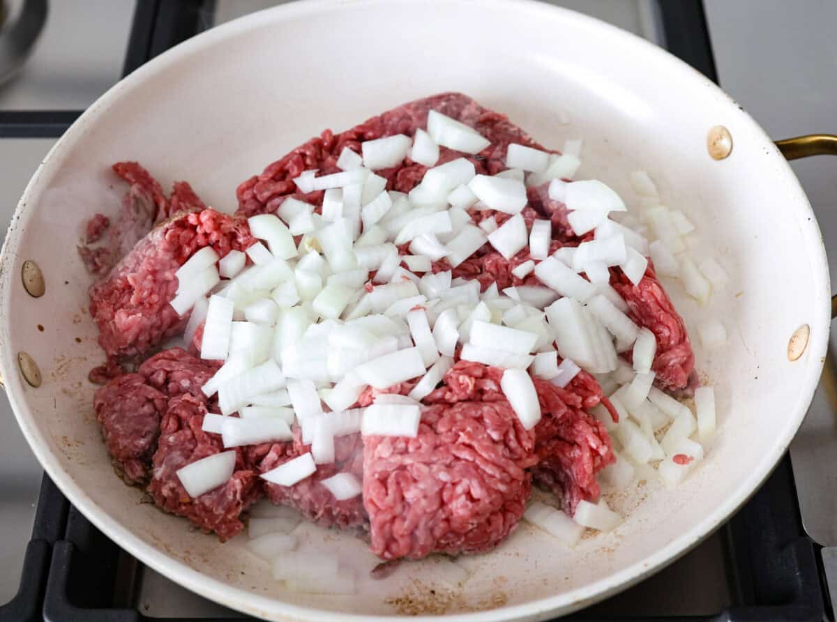 Hamburger Potato Casserole is hearty, filling, and great for family dinners. It's full of tender potatoes and ground beef, smothered in a deliciously creamy sauce, and covered in melty cheese. Overhead shot of ground beef and onions cooking in a skillet.